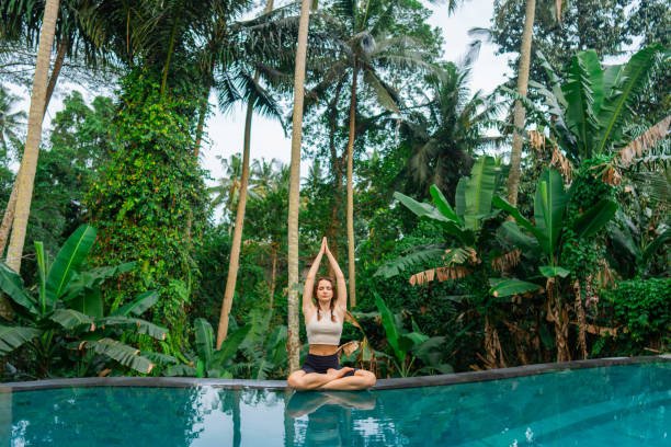 Woman doing yoga  near the swimming pool among jungles